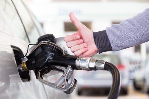 Petrol or gasoline being pumped into a motor vehicle car. Closeup of mans hand showing thumb up gesture, pumping gasoline fuel in car at gas station. Black and white image.