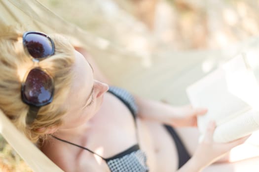 Woman reading book in hammock on the beach. Summertime read.