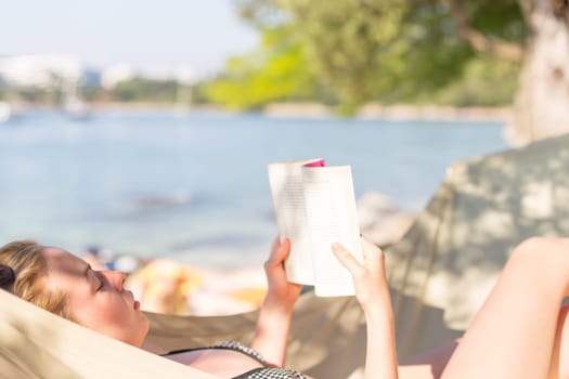 Woman reading book in hammock on the beach. Summertime read.