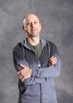 young smiling man with crossed arms in front of gray background