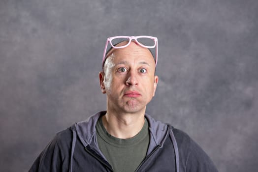 young man with pink glasses looking amazed in to the camera