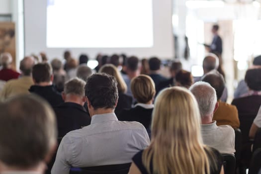 Speaker giving a talk in conference hall at business event. Audience at the conference hall. Business and Entrepreneurship concept. Focus on unrecognizable man in the audience.