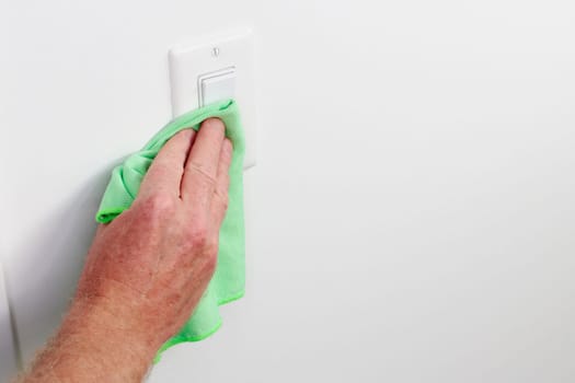White panel light control cleaning by hand cloth. Male hand dusting light switch with cleaning cloth Flat white light switch control being dusted and cleaned with a green cloth by a caucasian male hand
