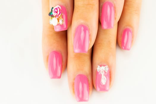 Closeup of beautiful pink nail design at female fingers on white background. Two figure on the nails decorate the pink nail design. Fashion nail design manicure.