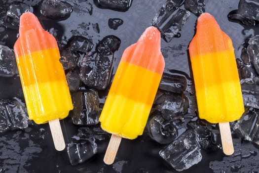 Fruit ice cream on stick over ice on black slate board. Focus on Popsicles.