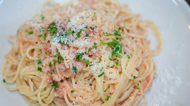 Close-up image of spaghetti sauce tarako which made from fresh cod fish in Japan and mixed with Thai coriander on the top of white plate and very famous italian-japanese menu dish in Thailand restaurant.