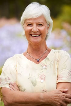 Portrait Of Senior Woman Enjoying Walk By Flower Beds In Park