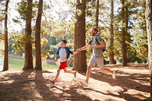 Father And Son On Hiking Adventure Running Through Forest