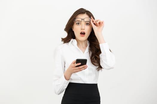 Business Concept: Surprised youngwoman holding mobile phone and staring at it while standing against grey background.