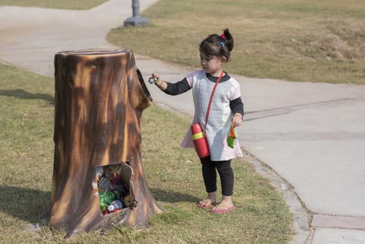 Cute little girl putting waste in the bin outdoor in a park.
