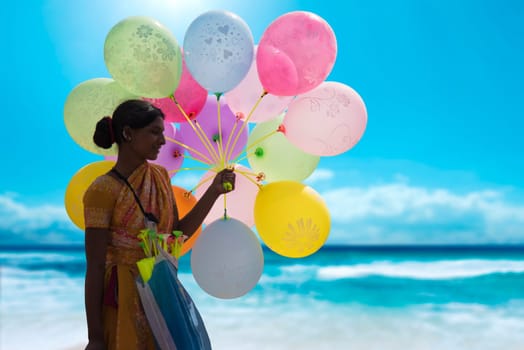 Indian hawker holding a bunch of colorful balloons at a beach and selling them to make a living.