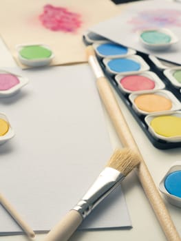 Set of watercolor paint, art brushes and paper on a desk