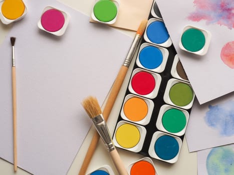 Set of watercolor paint, art brushes and paper on a desk