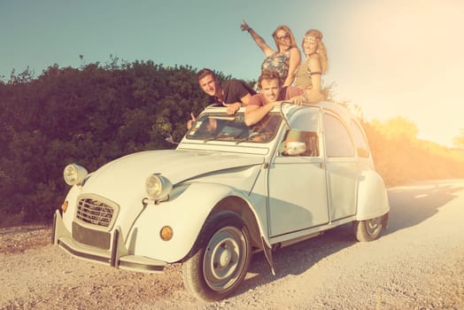 Group of happy friends in a car at sunset in summer.