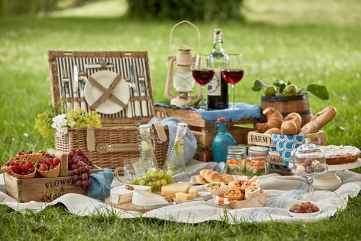 Gourmet picnic lunch for two in a lush green park with bread rolls, fresh berries, assorted cheese meat kebabs, pickles and red wine in stylish glasses on a hamper