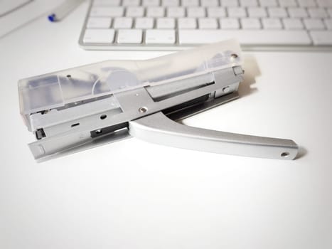 a modern stapler on a white desk with a keyboard in the background