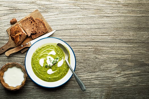 Fresh healthy green soup with cream served on wooden background