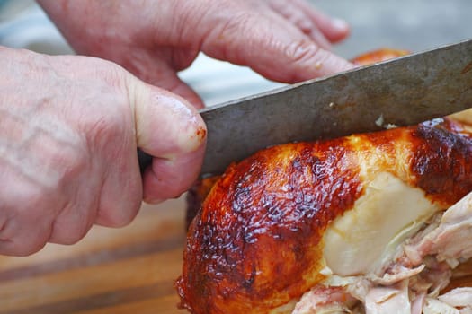 An older man slicing into a rotisserie chicken