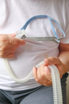 Man in an undershirt with the headgear and tubing part of a CPAP machine