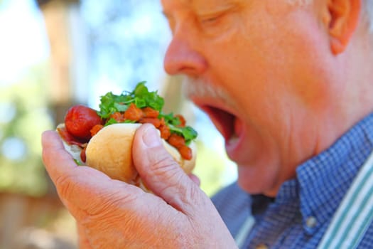 Man eating a hot dog topped with chili beans and chopped lettuce