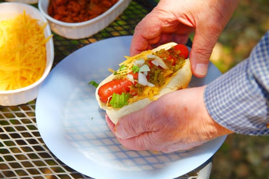 A man with a loaded hot dog in a backyard with dappled sunlight