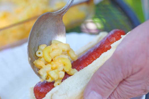 A man makes a mac ’n cheese dog outdoors