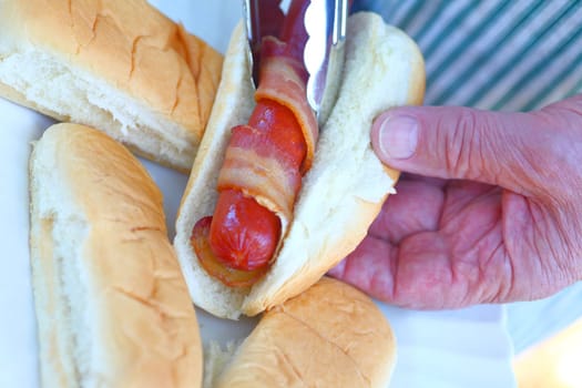 Overhead view of a man putting a bacon hot dog in a bun