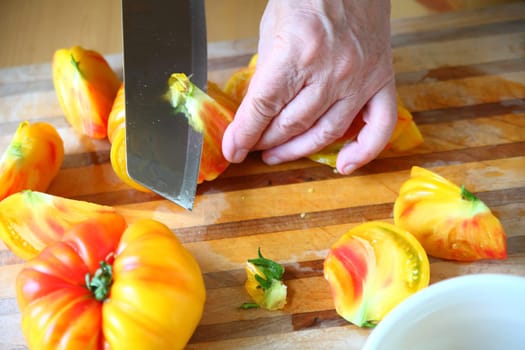 Yellow and orange-colored tomatoes with the hand of a man and a kitchen knife