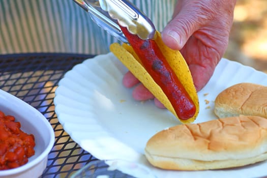 A man makes a taco dog with a dish of chili alongside