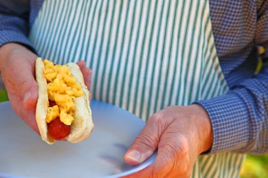 Man in apron with a hot dog topped with mac ’n cheese