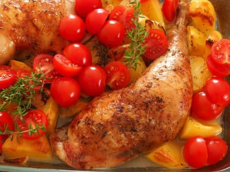 Tasty roasted chicken legs with fresh herbs and tomatoes in a glass pan
