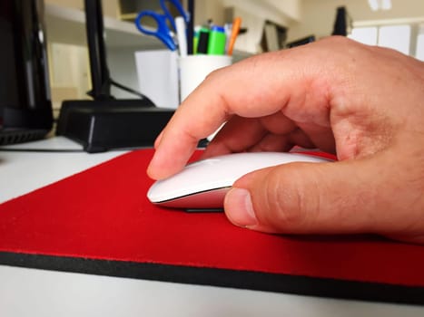 Male hand using a white computer mouse on a red mouse pad