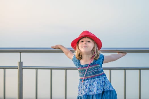 Cute little Caucasian girl holding on to a metal barrier on a seaside promenade in summer