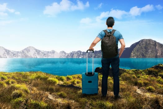 Back view of asian traveler man with suitcase enjoying lake view at mountain
