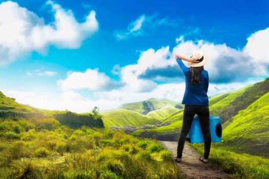 Back view of asian traveler woman with suitcase looking at green valley view at day