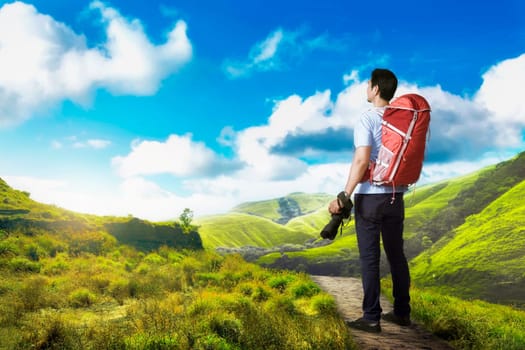 Attractive asian photographer man with camera on his hand on the green valley