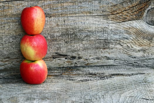 Three red fresh apples on a wooden surface