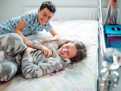 Little boy and his older sister are playfighting on a bed at home.