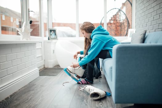 Little girl is putting figure skates on in the conservatory of her home before she goes to her skating lesson.