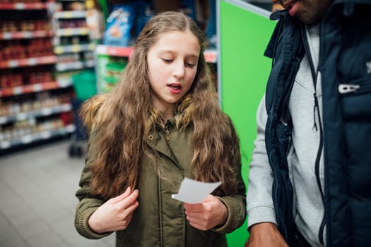 Little girl is reading things from a shopping list to her father in the supermarket.