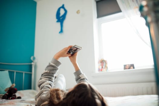 Little girl is lying on her bed, taking selfies on her smartphone.