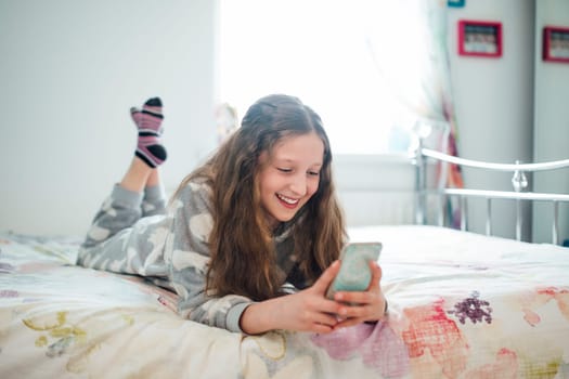 Little girl is lying on her bed, texting on a smart phone.