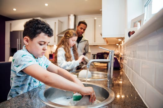 Little boy and his sister are helping dad with the washing up at home.