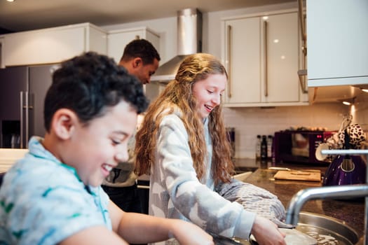 Little girl and her younger brother are doing the dishes after breakfast at home.