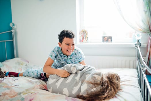Little boy and his older sister are playfighting on a bed at home.