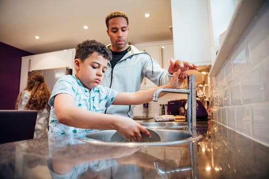 Little boy and his father are washing the dishes together at home.