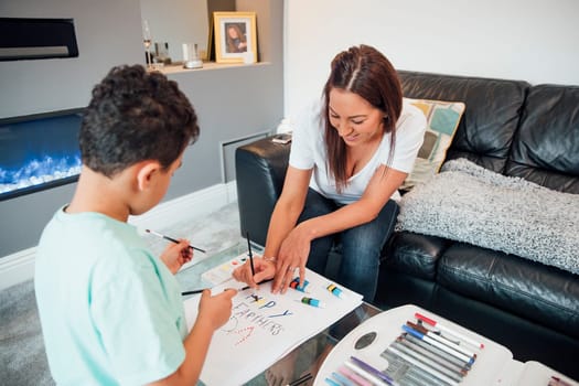 Little boy and his mother are making a Father's Day card at home using crayons and paints.