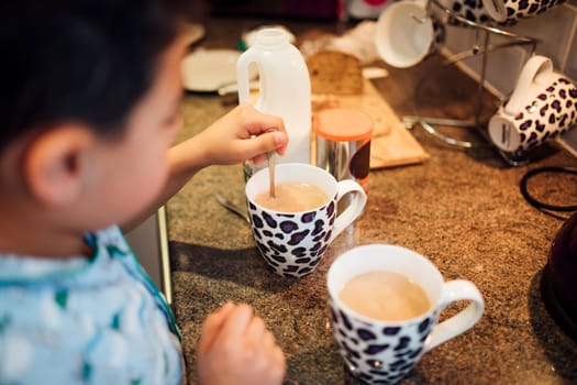 Little boy is helping his dad make tea in the morning. He is mixing the tea with a spoon.