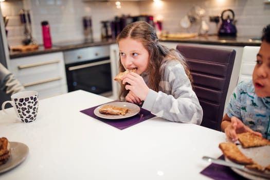Little girl is taking a bite of toast while having breakfast with her family at home.