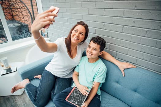 Mother and her son are taking a selfie while reading in the conservatory at home.